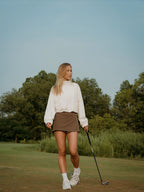 Woman on a golf course holding a golf club with trees in the background