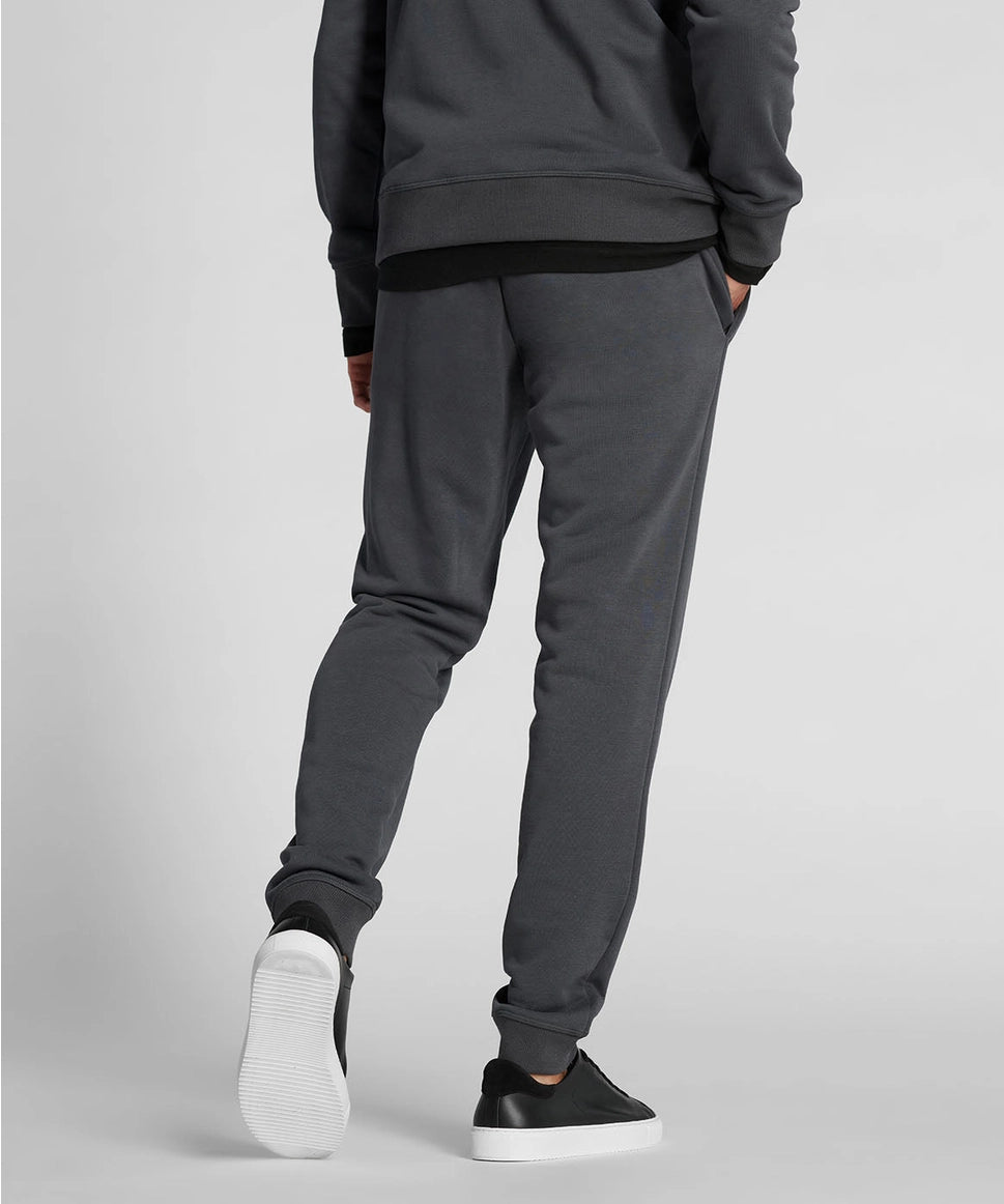 Man wearing dark gray sweatpants and black shoes on a light gray background RYU