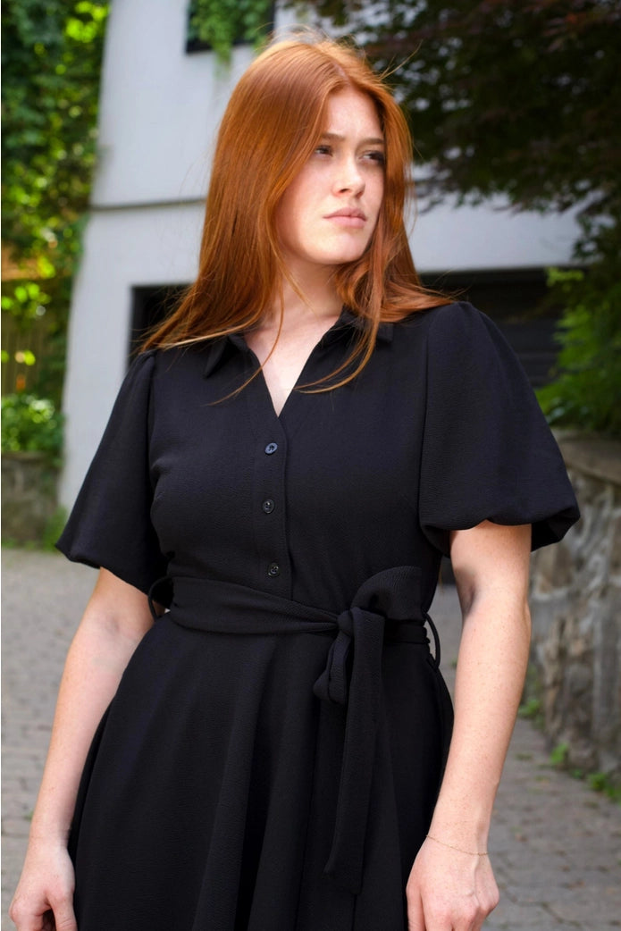 Woman wearing a black dress with short sleeves in an outdoor setting ANNICK