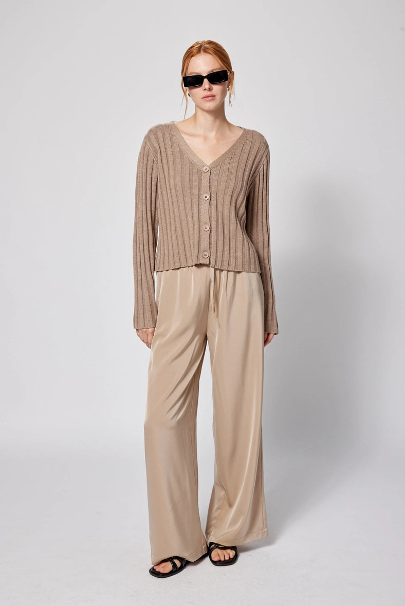 Woman wearing a beige cardigan and pants with sunglasses on a white background Amanda Maria