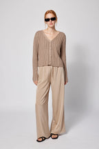 Woman wearing a beige cardigan and pants with sunglasses on a white background Amanda Maria