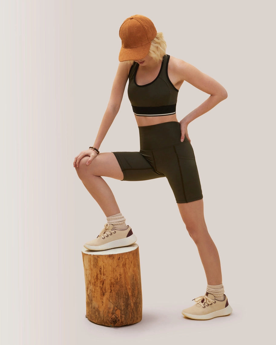 Women wearing a black sports bra and shorts with a brown cap, standing on a wooden block against a plain background. Rose Boreal