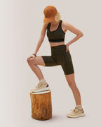 Women wearing a black sports bra and shorts with a brown cap, standing on a wooden block against a plain background. Rose Boreal
