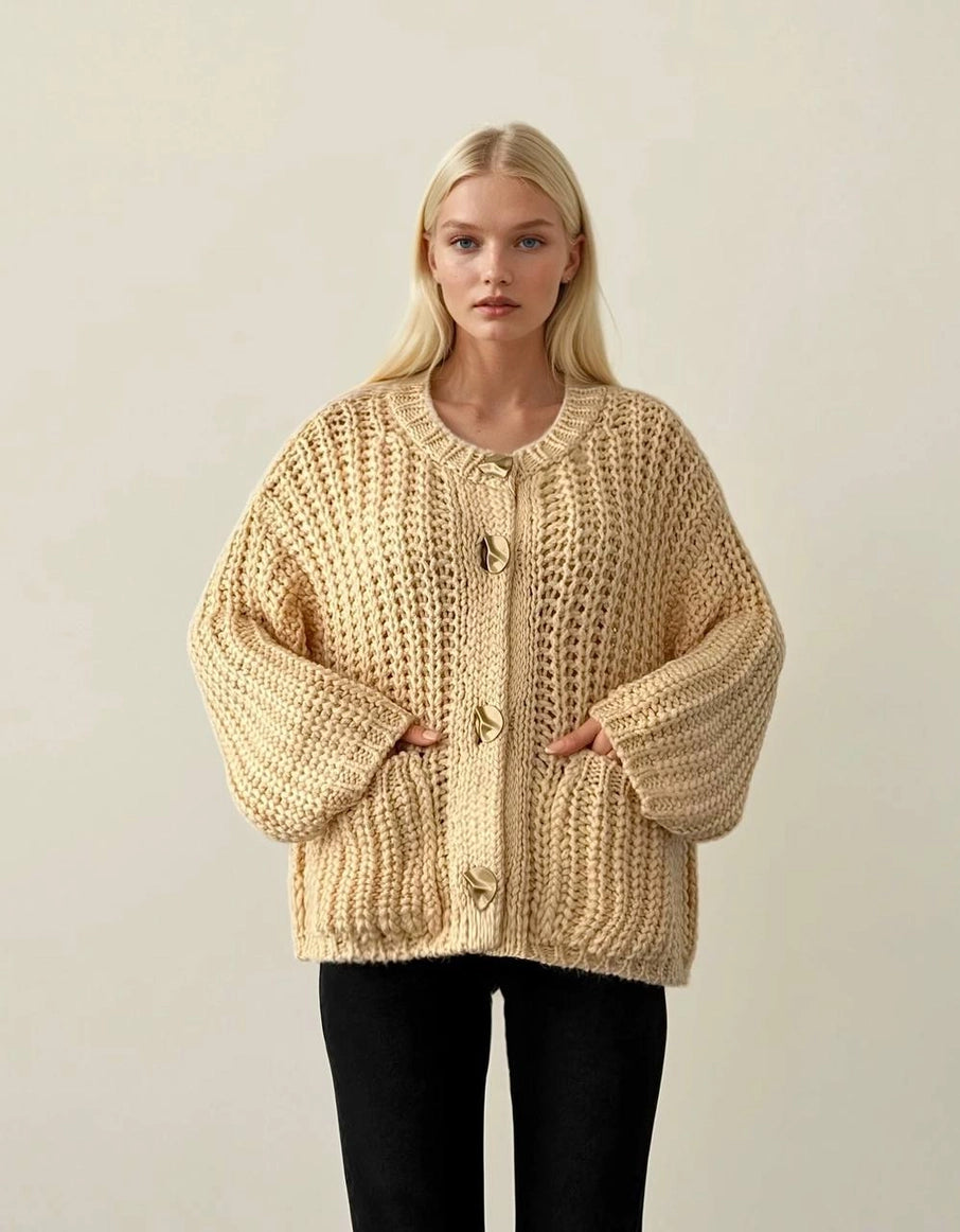 Woman wearing a beige chunky knit cardigan against a plain background ANAZ