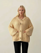 Woman wearing a beige chunky knit cardigan against a plain background ANAZ