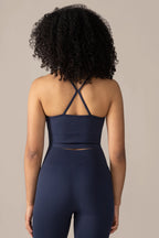 wome wearing a navy blue athletic outfit with criss-cross straps on a neutral background