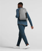 Man wearing a gray backpack walking on a plain background RYU