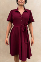 Woman wearing a burgundy dress with a belt against a beige background ANNICK