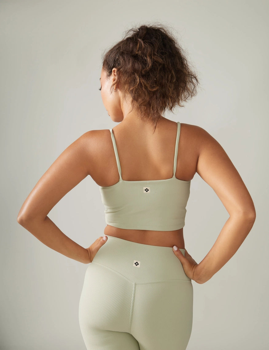 Woman wearing a light green sports bra and leggings against a neutral background Rose Boreal