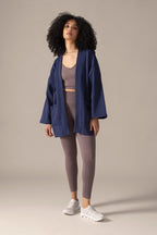 Woman wearing a blue jacket and brown outfit sitting on the floor against a beige background