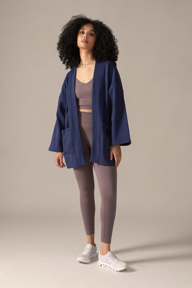 Woman wearing a blue jacket and brown outfit sitting on the floor against a beige background