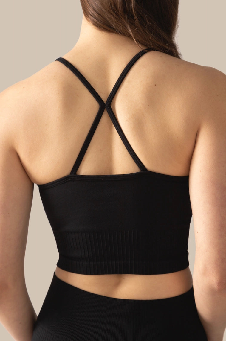 Black sports bra with criss-cross straps worn by a person on a neutral background
