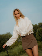 Woman in a white jacket and brown skirt standing outdoors with trees in the background in a brown BOV skort