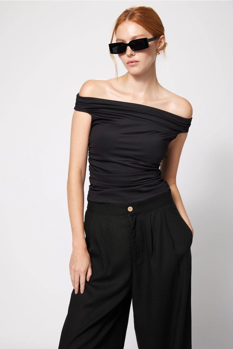 Woman wearing a black off-shoulder top and wide-leg pants against a white background Amanda Maria