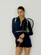 Woman in a navy blue tennis dress holding a tennis racket against a white background