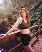 Woman in athletic wear standing on a wooden bridge in a forest setting Rose Boreal
