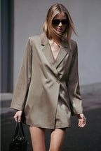 Woman wearing a beige trench coat and sunglasses, holding a black handbag.  Amanda Maria