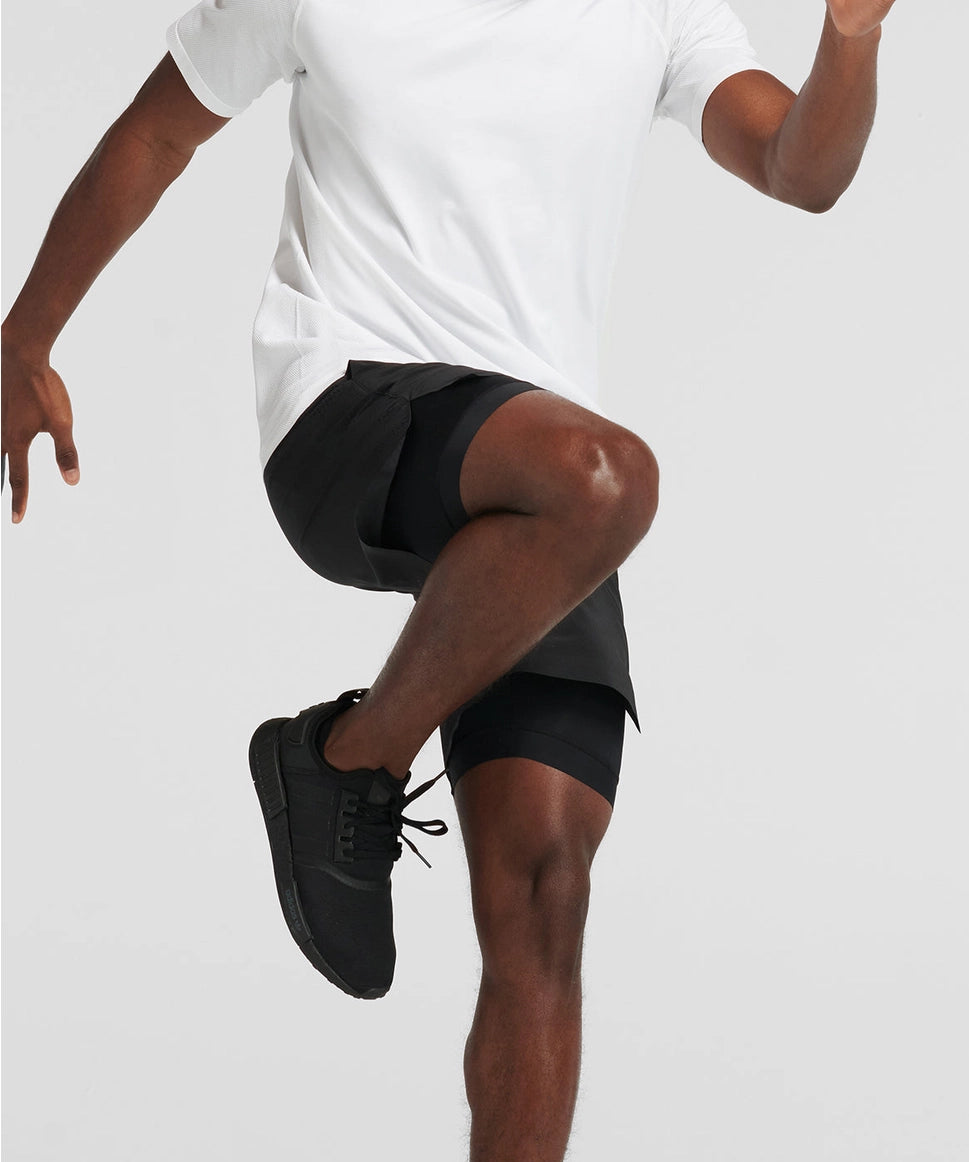 Man wearing black athletic shorts and black sneakers on a light gray background RYU