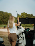 Woman loading golf clubs into a cart on a golf course in a brown BOV skort