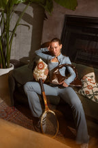 Woman sitting on a couch holding a vintage tennis racket in a cozy living room.