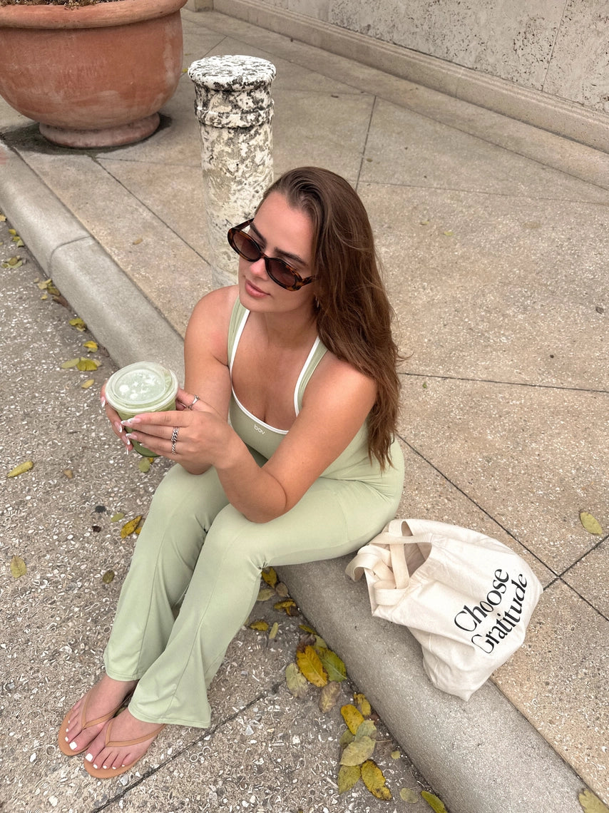 Woman in mint green outfit sitting on a curb with a bag and drink.
