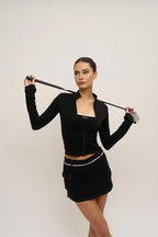 Woman in black outfit holding a golf club against a plain background