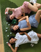 Three women lying on a green surface with golf balls around them