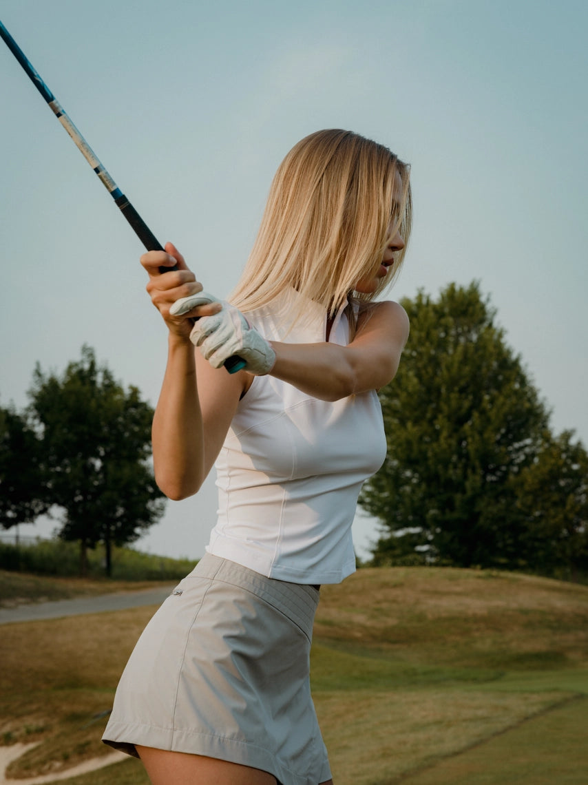 Woman playing golf on a course with trees in the background in a grey BOV skirt