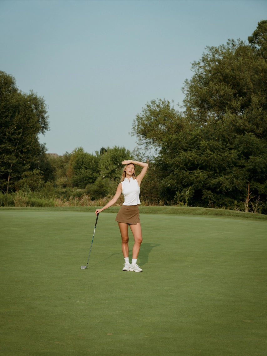 Woman on a golf course with trees in the background in a brown BOV skort