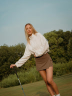 Woman on a golf course holding a club with trees in the background