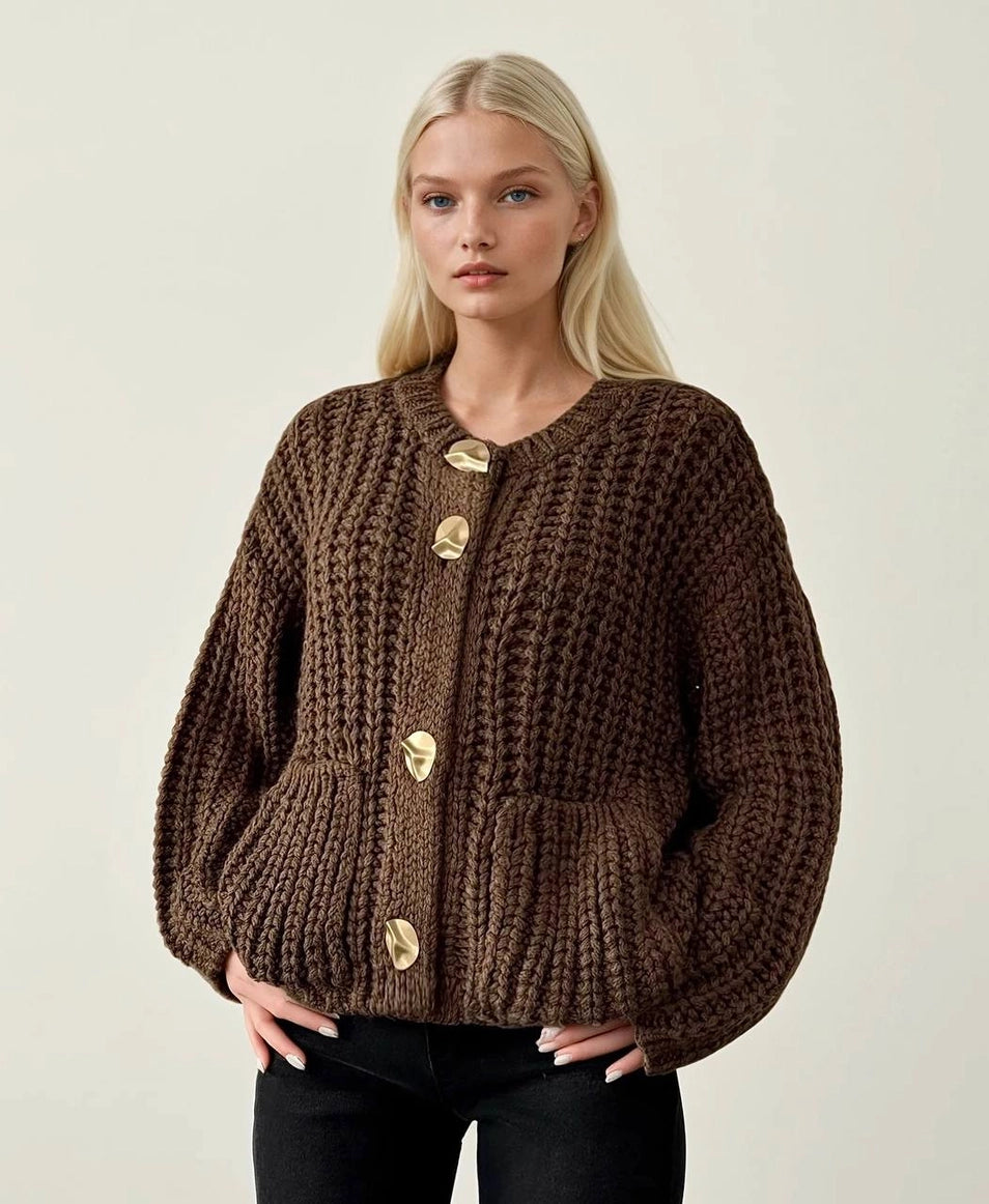 Woman wearing a brown knitted cardigan with gold buttons on a plain background ANAZ