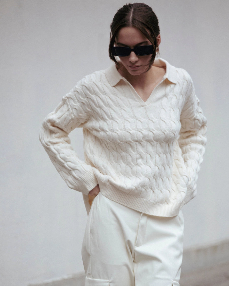 Women wearing a white cable knit sweater and white pants against a plain background Amanda Maria