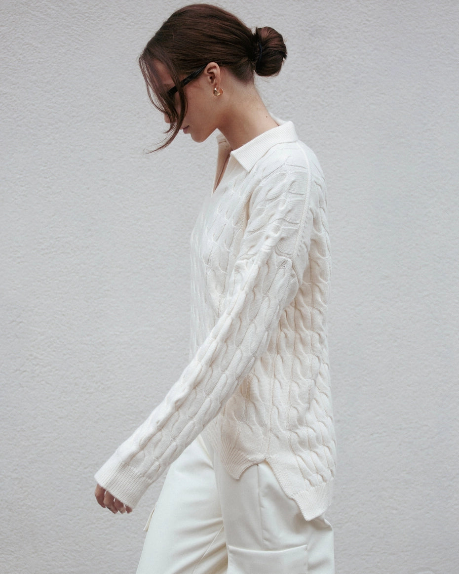 Woman wearing a white cable knit sweater against a plain background Amanda Maria