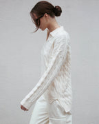 Woman wearing a white cable knit sweater against a plain background Amanda Maria