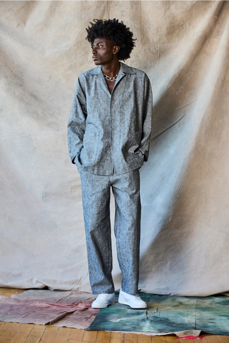 Man wearing a gray outfit standing against a textured beige backdrop Devlyn van Loon