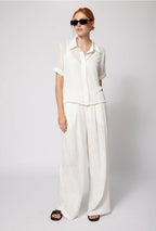 Woman wearing a white outfit with sunglasses on a plain background Amanda Maria