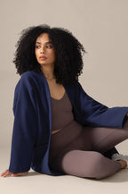 Woman wearing a blue jacket and brown outfit sitting on the floor against a beige background