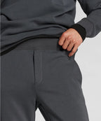 Man wearing dark gray sweatpants and a matching hoodie on a light gray background RYU