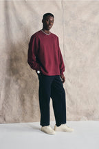 Man wearing a burgundy sweater, navy pants, and white shoes against a beige wall. Devlyn van Loon