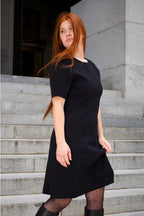 Woman wearing a black dress standing on stone steps. ANNICK