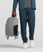 Person holding a gray backpack wearing a blue jacket and pants on a light gray background RYU