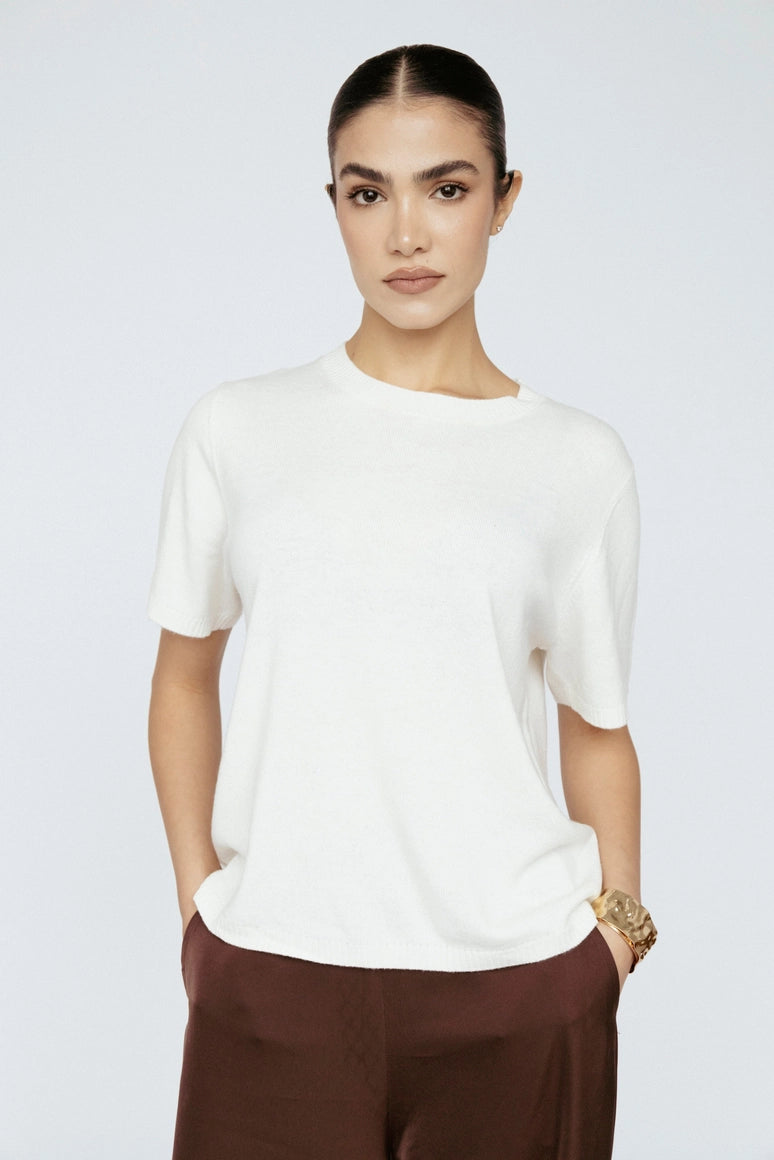 Woman wearing a white t-shirt and brown pants on a light gray background Amanda Maria
