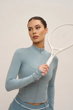 Woman in a light blue athletic outfit holding a tennis racket against a plain background