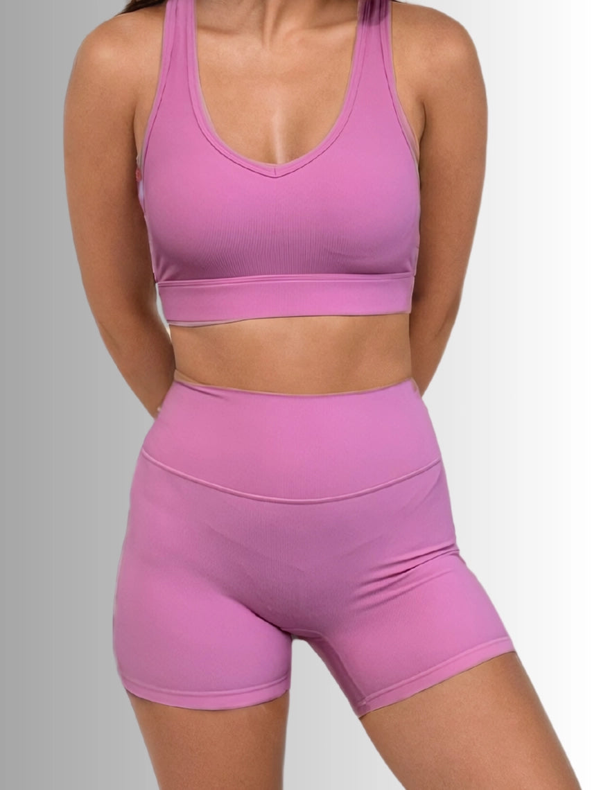 Women wearing a pink sports bra and shorts set on a gray background PRIV