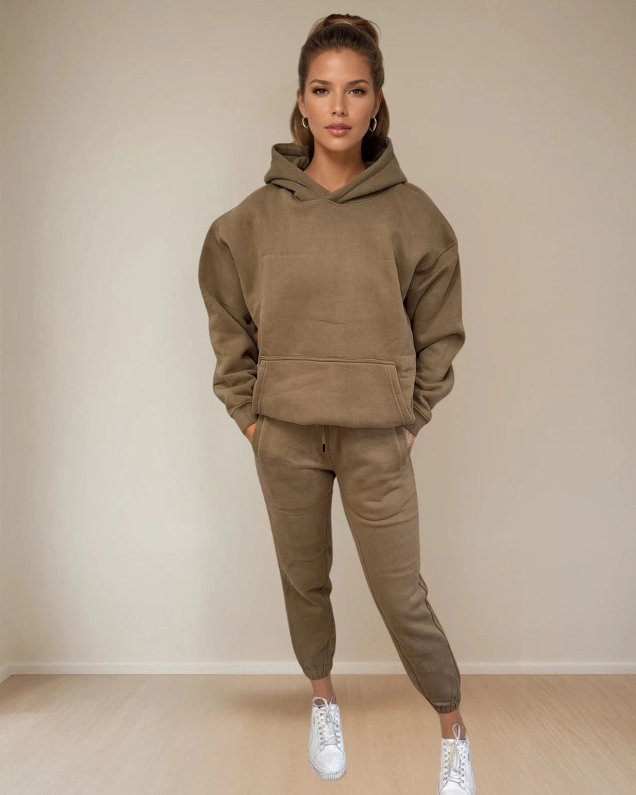 Woman wearing a brown hoodie and pants set with white sneakers against a beige background PRIV