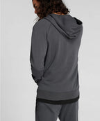 Person wearing a gray hoodie and pants on a light gray background RYU