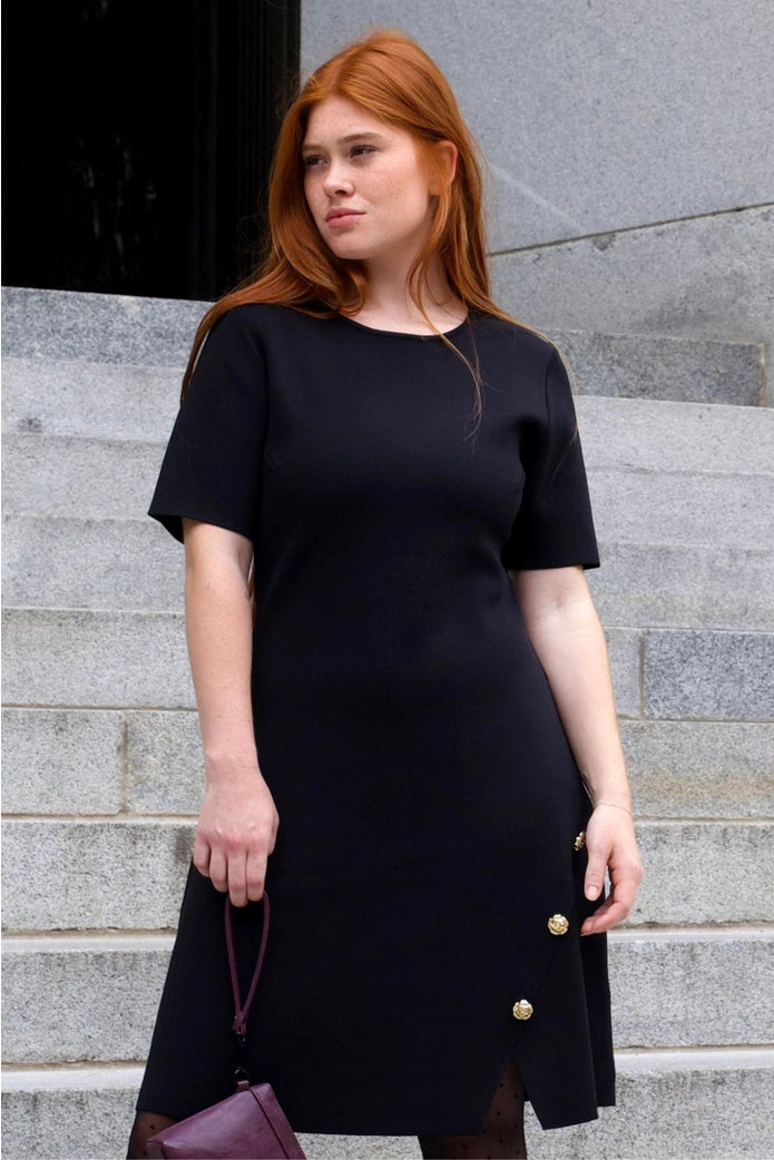 Woman wearing a black dress with gold buttons on gray steps ANNICK