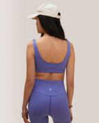 Woman in Rose Boreal purple athletic wear and cap standing outdoors with white  background