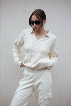 Person wearing a white cable knit sweater and pants against a plain background Amanda Maria