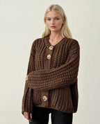 Woman wearing a brown knitted sweater with gold buttons on a plain background ANAZ